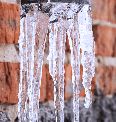 A close up of icicles hanging from the side of a brick wall.